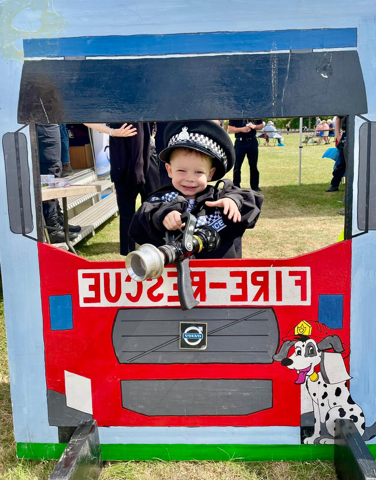 Young boy dressed up in police uniform having his picture taken in the wooden fire engine